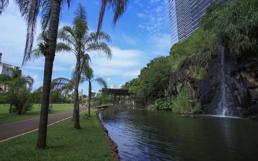 Lago, pista e cachoeira entre as árvores do Parque Raya